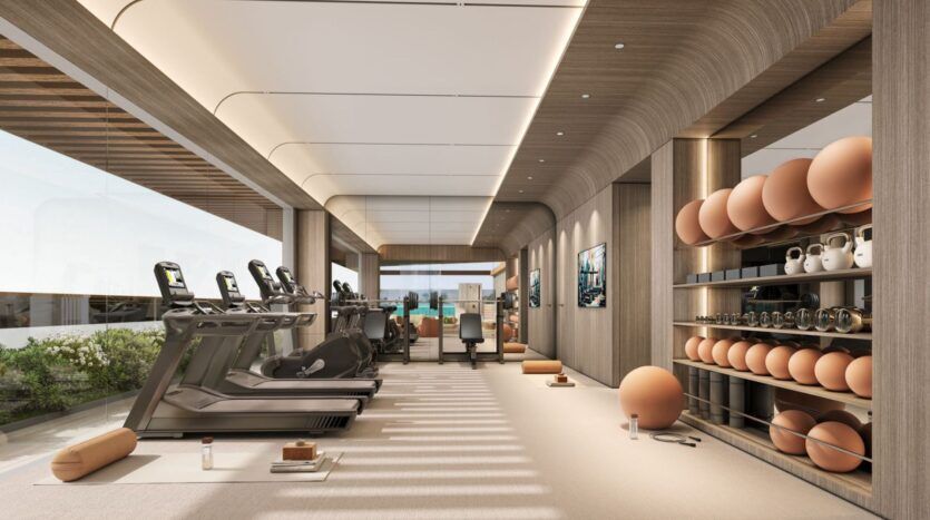 La salle de sport moderne de Derby Heights est équipée de tapis roulants, de vélos d'appartement et d'étagères contenant des kettlebells, des ballons de yoga et des tapis. De grandes fenêtres inondent l'espace épuré et minimaliste de lumière naturelle et laissent entrevoir les plantes luxuriantes qui poussent à l'extérieur.