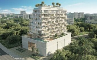 Un immeuble moderne de plusieurs étages avec des balcons et des jardins sur les toits, entouré d'arbres luxuriants et de verdure, se dresse dans la ville de Meriden, avec d'autres bâtiments visibles à l'arrière-plan.