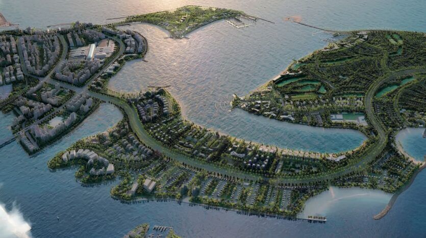 Vue aérienne d'une ville côtière avec des espaces verts, des routes sinueuses et des résidences Meriden Beach sur plusieurs îles entourées d'eau, reliées par des ponts, sous un soleil couchant.