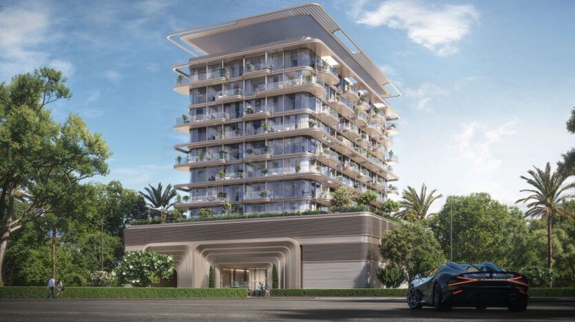 Un bâtiment moderne de plusieurs étages avec de grands balcons et de la verdure est entouré d'arbres et de palmiers. Au premier plan, une voiture de sport élégante est garée sous un ciel bleu clair, reflétant le luxe de The Tides by Amis.