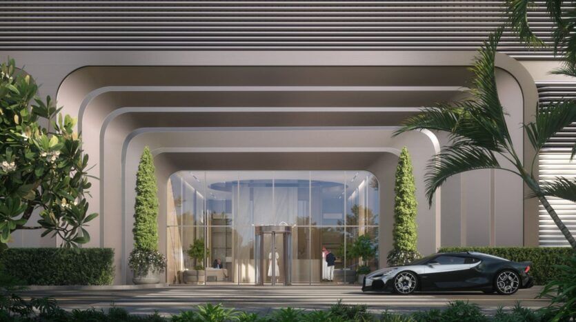 L'entrée du bâtiment moderne de The Tides by Amis présente des lignes architecturales courbes, de grandes portes vitrées, de hautes plantes vertes et une élégante voiture de sport noire garée devant, le tout entouré d'une végétation luxuriante.