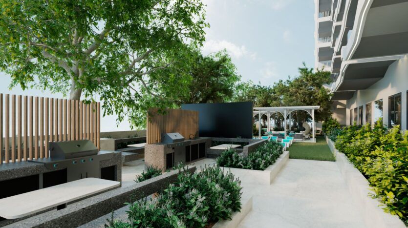 Terrasse moderne avec grilles de barbecue Reef 996, comptoirs en pierre, bancs, plantes vertes luxuriantes, pelouse et un coin salon ombragé sous des pergolas blanches à côté d'un bâtiment contemporain lors d'une journée ensoleillée.
