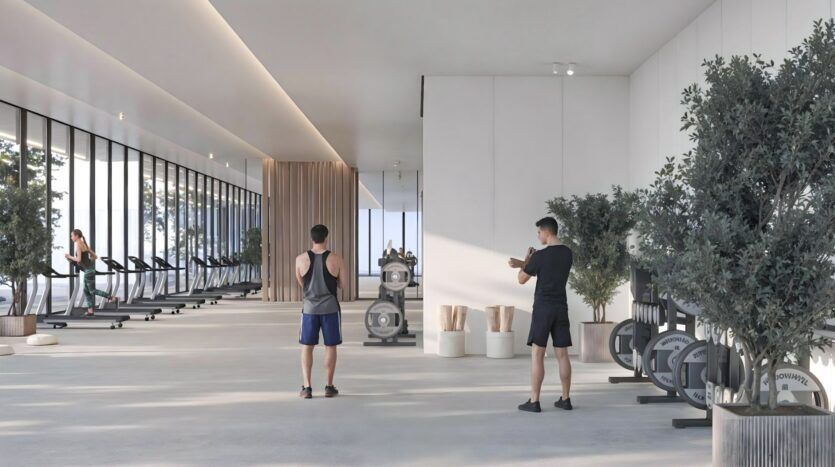 Une salle de sport moderne et spacieuse dans Sakura Gardens avec de grandes fenêtres, plusieurs tapis de course sur la gauche, des appareils d'haltérophilie, deux personnes faisant de l'exercice et des plantes en pot dans tout l'espace propre et minimaliste.