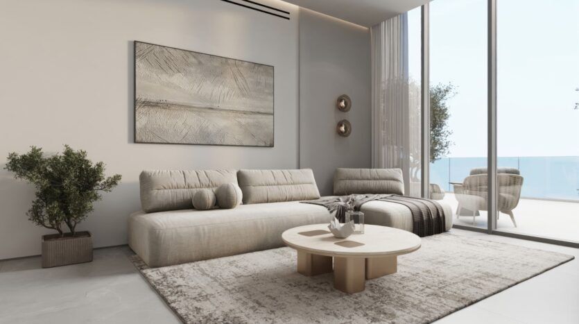 Un salon moderne avec un canapé sectionnel beige, une table basse ronde, des œuvres d'art murales abstraites et un décor neutre, inspiré des jardins de Sakura. De grandes portes vitrées s'ouvrent sur un balcon où l'on peut s'asseoir en plein air et qui offre une vue imprenable sur l'océan.