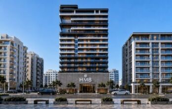Le Beverly Crown, un gratte-ciel moderne signé HMB, se dresse fièrement, avec son enseigne emblématique, au milieu d'immeubles d'habitation de hauteur moyenne, d'arbres et d'une circulation animée. Des bancs et le trottoir agrémentent le premier plan sous un ciel bleu limpide.