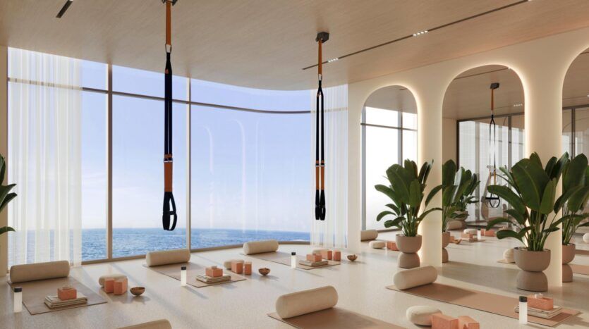 Un studio de yoga spacieux et moderne, doté de baies vitrées donnant sur l'océan, situé à Vue Dorée, avec des plantes en pot, des tapis, des coussins de yoga, des blocs de yoga, des bouteilles d'eau et deux sangles de suspension accrochées au plafond.
