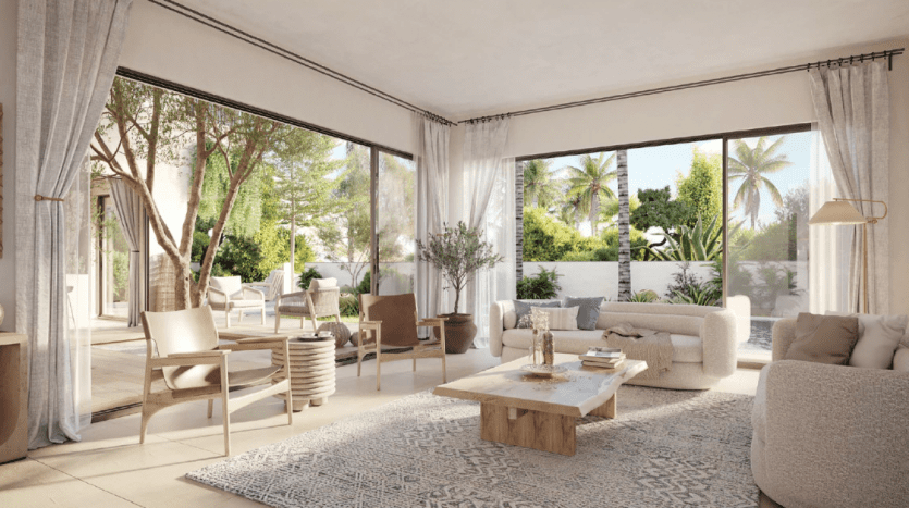 A serene living room in a Dubai apartment opens onto a sunny garden patio, featuring comfortable beige furniture, a neutral carpet and large windows that show off the lush greenery outside.
