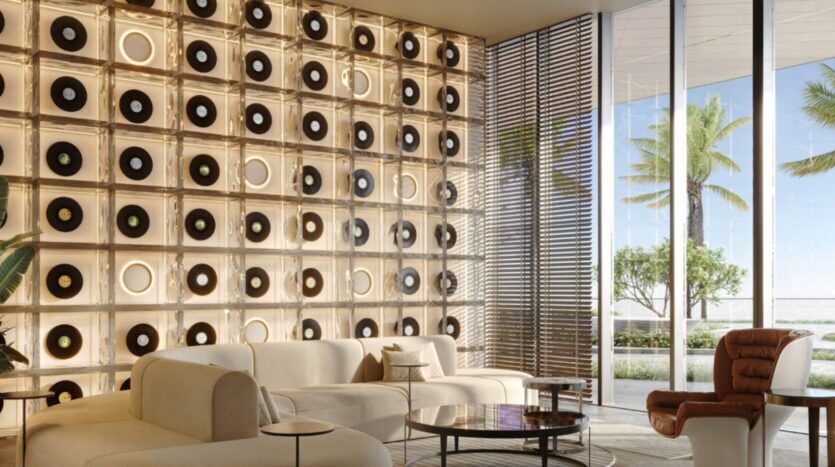 Le salon moderne des Mövenpick Residences est aménagé avec des canapés couleur crème, un fauteuil marron, des tables rondes et un mur décoratif orné de disques vinyles lumineux. Les baies vitrées offrent une vue sur les palmiers et un paysage extérieur baigné de lumière.