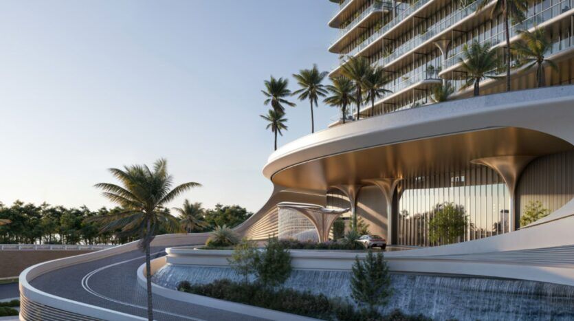 Un bâtiment moderne à l'architecture courbe et vitrée, doté de hauts piliers et entouré de plusieurs palmiers. Une voiture remonte l'allée sinueuse menant aux Mövenpick Residences, bordée d'espaces verts aménagés sous un ciel dégagé.