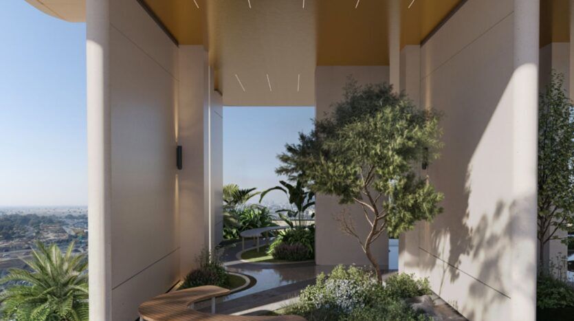 Terrasse en plein air couverte, agrémentée de hautes colonnes, au sein des Mövenpick Residences, dotée de bancs modernes et d'une végétation luxuriante composée d'arbres et de plantes. En arrière-plan, le paysage urbain et le ciel bleu sont visibles à travers de grands espaces ouverts.