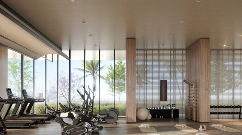 Salle de sport moderne au Mövenpick Residences, équipée de tapis de course, de vélos d'appartement, d'haltères, de tapis de yoga et d'appareils de fitness. De grandes baies vitrées donnent sur les palmiers et la verdure à l'extérieur, inondant de lumière naturelle cette salle spacieuse au style minimaliste.