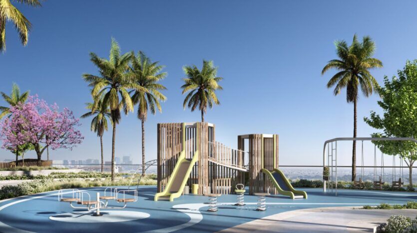 Une aire de jeux moderne, équipée de toboggans, de structures d'escalade et de jeux à ressort, se trouve au bord de l'eau près des résidences Mövenpick, entourée de palmiers sous un ciel bleu limpide, avec la silhouette de la ville visible au loin.