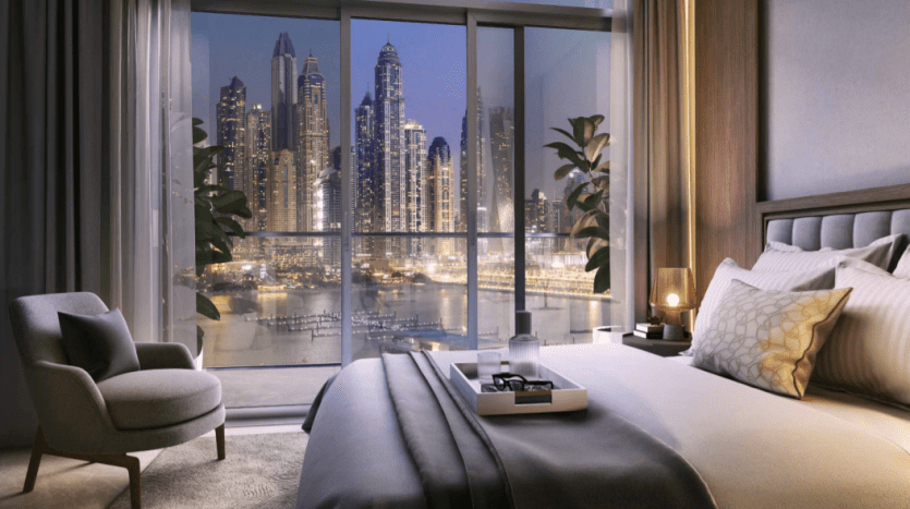 Une chambre luxueuse dans une résidence de palais avec une grande fenêtre offrant une vue panoramique sur les toits de la ville illuminés la nuit, avec des gratte-ciel modernes. La chambre est élégamment meublée avec un confortable