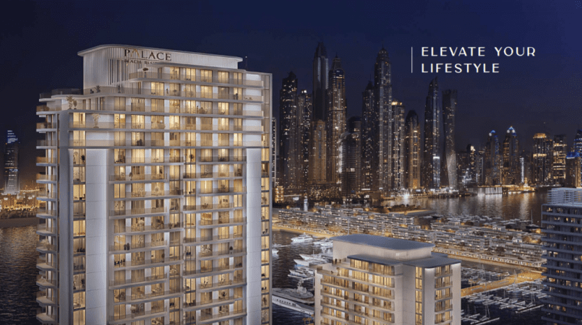 Vue nocturne de la Palace Beach Residence, un immeuble de luxe de grande hauteur avec le texte « élevez votre style de vie » sur l'horizon d'une ville moderne avec des bâtiments illuminés et une marina.