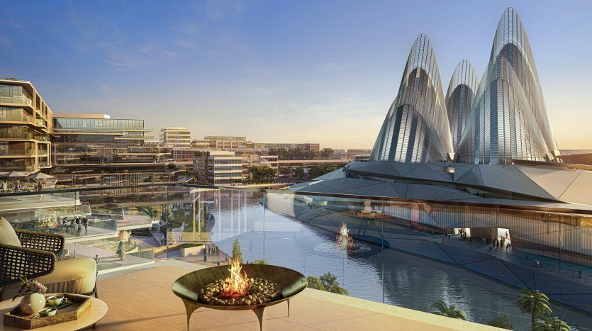 Paysage urbain futuriste au coucher du soleil avec des bâtiments et des tours modernes se reflétant dans un plan d'eau. Le premier plan montre la terrasse d'un luxueux appartement à Dubaï avec un foyer, surplombant la scène.