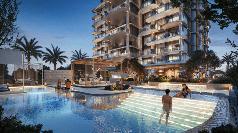 Un immeuble d'appartements moderne avec balcons donne sur une luxueuse piscine extérieure. Les gens se détendent au bord de la piscine, certains dans l'eau. Les palmiers et l'éclairage d'ambiance rehaussent le cadre nocturne du Vitalia, faisant écho à l'élégance de Palm Jumeirah.