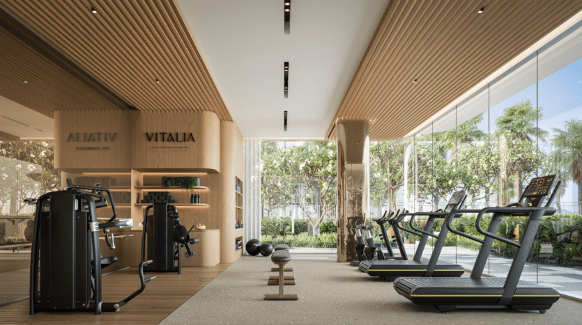 La salle de sport moderne Vitalia de Palm Jumeirah est dotée de grandes fenêtres abritant des tapis de course, des appareils de musculation et des bancs. Les boiseries et la verdure créent une atmosphère ouverte et accueillante où la lumière naturelle met en valeur le design spacieux.
