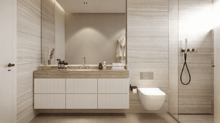 Modern bathroom featuring a large vanity with white cabinetry and wood accents, wall-mounted toilet and glass shower stall. Neutral tones and clean lines dominate the space in this Dubai apartment.