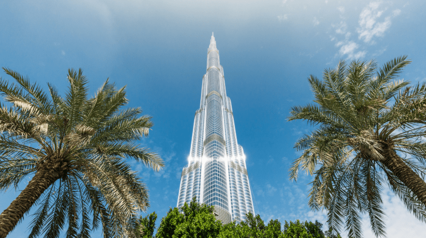 Una suggestiva vista del Burj Khalifa incorniciato da due palme sotto un cielo azzurro e limpido, che mette in risalto l'offerta mozzafiato degli immobili di Dubai. La luce del sole si riflette sull'elegante superficie metallica dell'edificio.