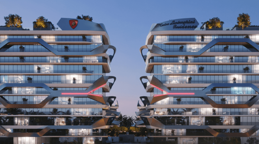 Two modern, multi-storey residential buildings with bay windows and angular architectural designs stand side by side, adorned with greenery on their roofs. Both buildings prominently display the "Tonino Lamborghini Residences Dubai" label on their facades. The sky is a twilight hue.