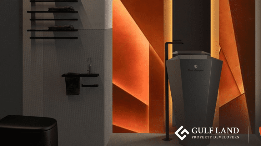 A modern interior bathroom at Tonino Lamborghini Residences Dubai with elegant, dark surfaces and a unique angled pedestal sink set against a dramatic geometric wall in warm tones. Towels and toiletries are neatly arranged. The "GULF LAND PROPERTY DEVELOPERS" logo is displayed in the lower right-hand corner.