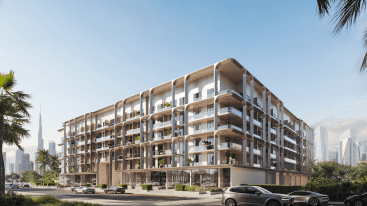 Un immeuble d'appartements moderne à plusieurs étages avec de grandes fenêtres et des balcons, entouré de palmiers, rappelant le One Beverly Dubai. Plusieurs voitures sont garées le long de la rue devant lui, et un horizon urbain avec des immeubles de grande hauteur est visible en arrière-plan sous un ciel bleu.