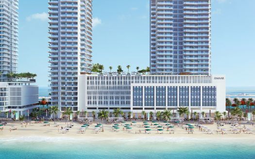 Un complejo de lujo con vistas al puerto deportivo con tres grandes edificios, palmeras, una playa de arena abarrotada con sombrillas de colores y un cielo azul despejado.