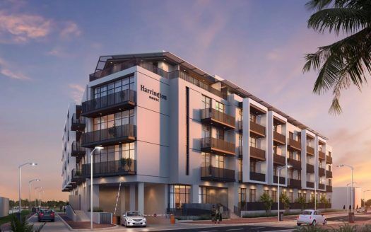 Edificio de apartamentos Harrington House al atardecer con los interiores iluminados, varios balcones visibles, una palmera a la izquierda y coches aparcados a lo largo de la calle.
