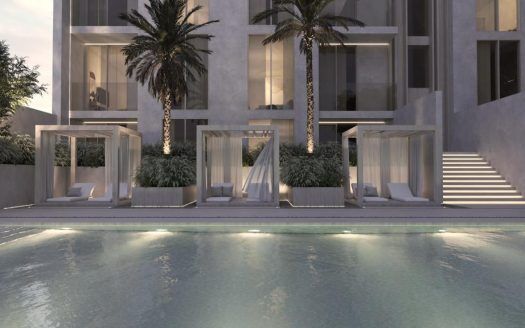 Una casa de arquitectura moderna con una piscina en primer plano con cabañas iluminadas y palmeras con el telón de fondo de un edificio de varias plantas por la noche, perfecta para los interesados en el sector inmobiliario de Dubai.