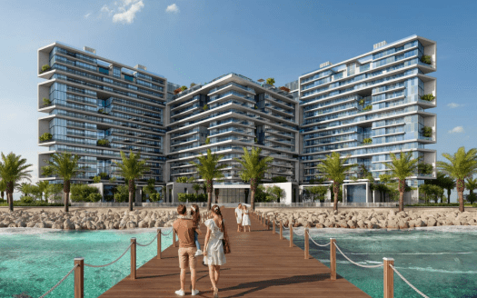 Modernos edificios residenciales de varias plantas en el paseo marítimo con exuberante vegetación en los balcones bajo un cielo azul despejado. En primer plano se ve un embarcadero de madera con gente caminando hacia el complejo. Ideal para inmobiliarias de Dubai
