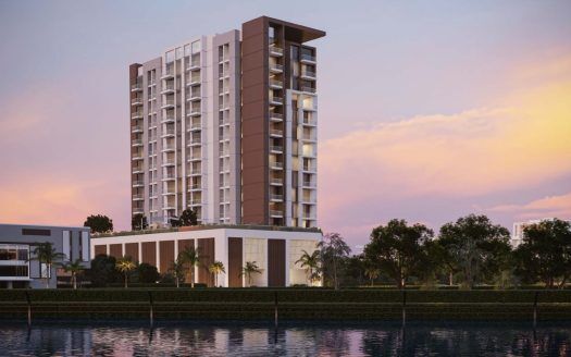 Un moderno rascacielos residencial al atardecer, con un cielo vibrante y reflejos en un tranquilo paseo marítimo, rodeado de exuberante vegetación, ilustra la primera línea inmobiliaria de Dubai.