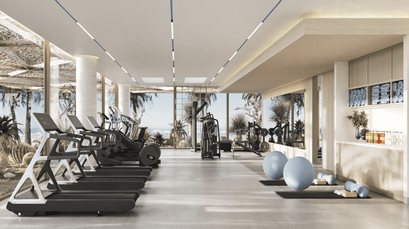 Intérieur de salle de sport luxueux avec tapis roulants, équipements d'haltérophilie et ballons d'exercice, donnant sur une plage tropicale à travers de grandes fenêtres. Un design moderne avec de la lumière naturelle et une opportunité d'investissement idéale dans l'immobilier à Dubaï