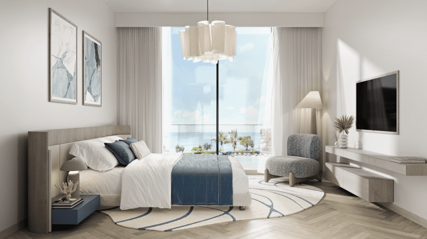 Chambre moderne dans un appartement de Dubaï comprenant un grand lit recouvert d'une literie bleue, une tête de lit en bois, une baie vitrée offrant une vue sur l'océan et une décoration minimaliste comprenant une télévision murale et des œuvres d'art.