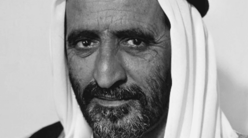 Portrait en noir et blanc d'un homme d'âge moyen barbu, portant un keffieh blanc traditionnel, regardant directement la caméra avec une expression subtile dans sa villa de Dubaï.