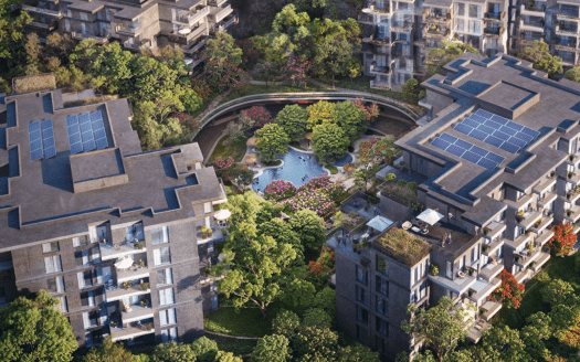 Vista aérea de un complejo residencial de lujo formado por varios bloques de pisos modernos con paneles solares en los tejados. El complejo está rodeado de exuberante vegetación, árboles y jardines paisajísticos enclavados en el sereno bosque de Ghaf, incluida una fuente central con vibrantes plantas en flor.