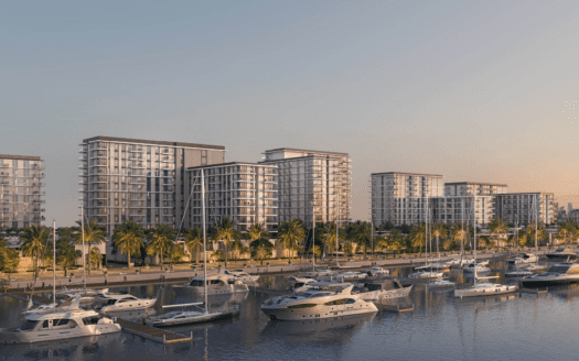 Una hilera de modernos apartamentos de gran altura con balcones dan a un puerto deportivo repleto de yates en Pierpoint. Las palmeras bordean el paseo marítimo y el horizonte distante de la ciudad es visible en un cielo despejado al atardecer.