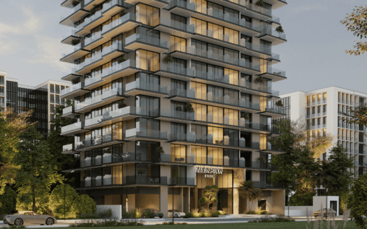 Moderno edificio residencial de varias plantas con grandes balcones acristalados, rodeado de árboles y vegetación, situado en el Arlington Park de Dubai. El interior está bañado por una luz cálida, con algunos coches aparcados delante y los edificios adyacentes visibles al fondo.