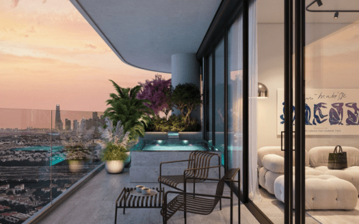 Un moderno balcón con balaustradas de cristal, plantas en macetas y una pequeña piscina ofrece vistas de la ciudad al atardecer. Dos sillas negras y una mesa están junto a un cómodo salón interior con asientos de felpa y obras de arte contemporáneo.