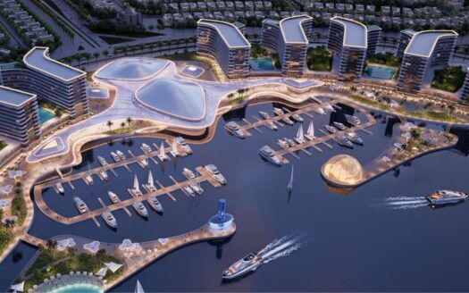 Vista aérea de River Cove Residences en la que se aprecia un moderno puerto deportivo con varios yates amarrados, edificios de formas singulares, caminos sinuosos y una estructura redonda de cristal junto al agua. Dos embarcaciones navegan por el puerto deportivo, rodeado de zonas verdes.