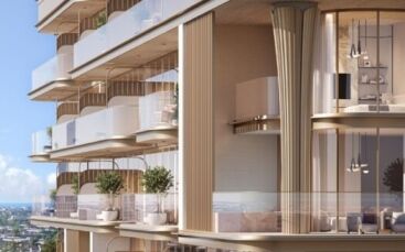 Le 113 Residences by Iman est un immeuble d'appartements de luxe moderne doté de vastes balcons en verre, de hautes fenêtres, d'un éclairage élégant et de plantes d'extérieur. Des tons neutres et chauds dominent la façade, avec des vues sur l'océan et la ville sous un ciel bleu limpide.