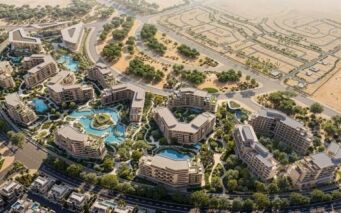 Vue aérienne d'Arancia Yards by Beyond, un complexe résidentiel moderne composé de plusieurs bâtiments, de jardins paysagers, d'allées sinueuses et de piscines bleues, entouré de verdure et de désert, avec des routes et des terrains non aménagés à proximité.