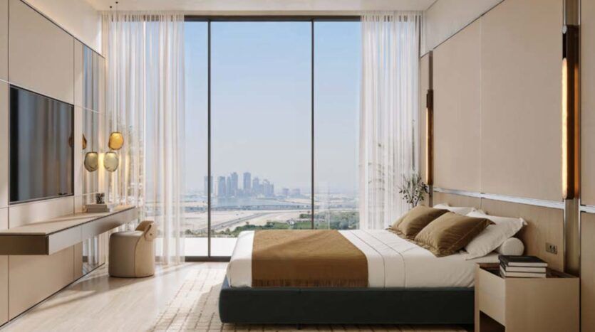 Chambre moderne à Binghatti Wraith, décorée dans des tons beiges et marron, avec un grand lit, une télévision, un bureau et une baie vitrée offrant une vue imprenable sur les toits de la ville et le front de mer. La lumière naturelle inonde cet espace minimaliste et élégant.