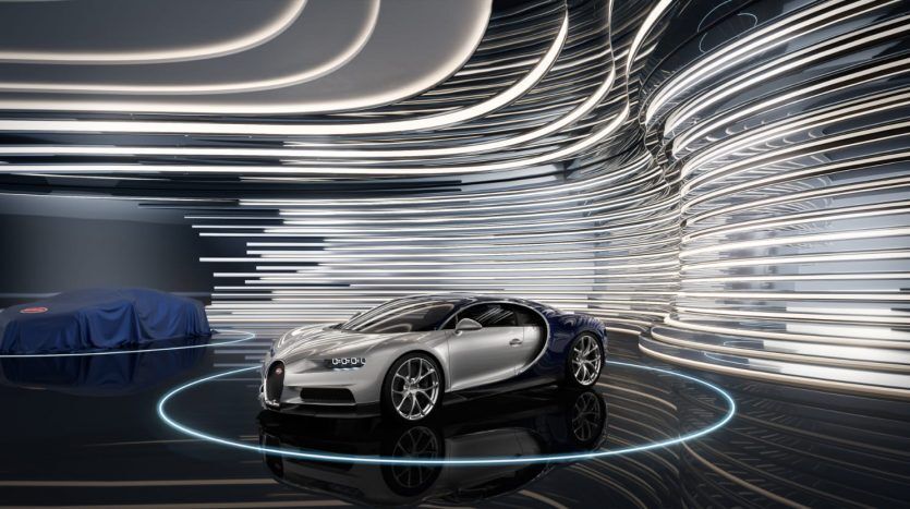 Un showroom futuriste avec une élégante voiture de sport argentée exposée, entourée de motifs lumineux dynamiques et tourbillonnants et une villa partiellement visible recouverte d'un tissu bleu en arrière-plan.