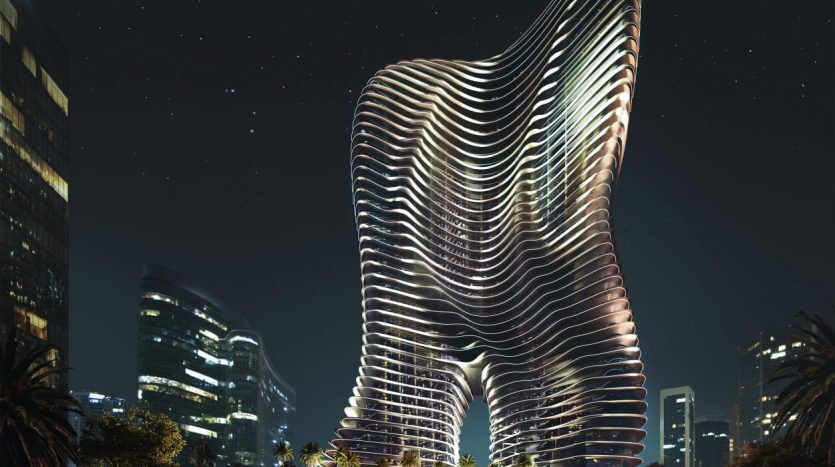 Un gratte-ciel futuriste la nuit, présentant un design ondulé unique éclairé par des lumières blanches, sur fond de paysage urbain et de ciel étoilé de Dubaï.