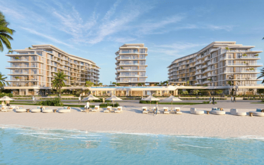 Un complexe balnéaire composé de deux bâtiments modernes à plusieurs étages entourés de palmiers. Des parasols blancs et des chaises longues sont disposés sur le rivage sablonneux, avec les vagues bleues calmes de l'océan au premier plan sous un ciel clair et ensoleillé.