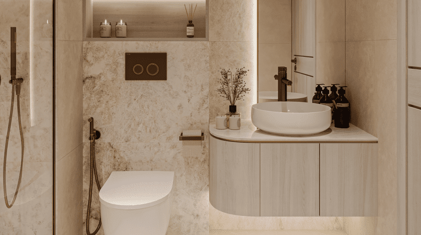 Salle de bains moderne avec murs en marbre beige, toilettes suspendues, robinetterie dorée et vasque ronde sur meuble-lavabo suspendu. Distributeurs de savon foncés, petites plantes et éclairage floarea créent une atmosphère chaleureuse et élégante.