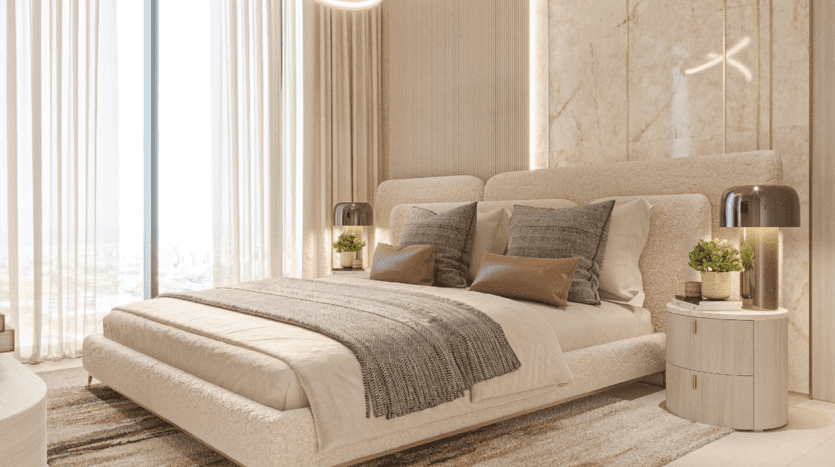 Chambre luxueuse sous un ciel ensoleillé avec un grand lit et des oreillers beiges et gris. Un mur en marbre orne le fond du lit, des tables de chevet rondes avec lampes et des plantes en pot. De grandes fenêtres avec des rideaux transparents laissent entrer la lumière naturelle.