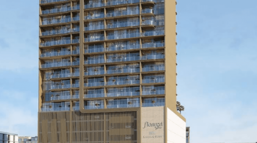 Un grand immeuble d'appartements moderne, doté d'une façade vitrée et de multiples balcons, se dresse sur un ciel étoilé. L'immeuble arbore des touches dorées et une enseigne au pied, dont le nom est illisible. Des palmiers sont visibles à son pied.