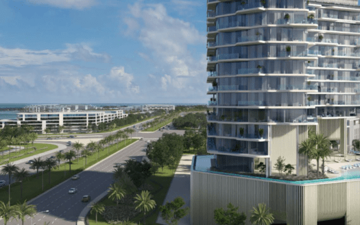 Un immeuble moderne de grande hauteur avec des balcons en verre surplombe une large route bordée de palmiers sur l'île d'Octa, sur l'île de Dubaï, avec des bâtiments plus contemporains et l'océan visibles en arrière-plan sous un ciel partiellement nuageux.