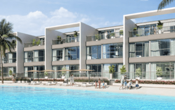 Des immeubles résidentiels modernes dotés de grands balcons surplombent un lagon bleu scintillant de Dubaï, entourés de palmiers et de personnes pratiquant diverses activités comme la natation et les bains de soleil.
